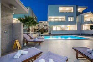 A modern building with a swimming pool, sun loungers, and a palm tree. - Double Room with Balcony and Pool (Novalja)