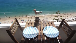 A balcony with wooden chairs and tables, overlooking a beach with people and a seagull. - Lingon Silver Apartment, Wifi, AC, Balcony (Sesimbra)