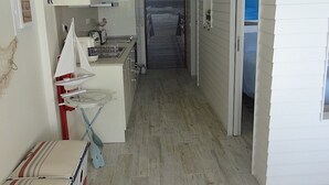A narrow hallway leading to a beach view, with a small kitchenette and a sailboat model on the left. - Lingon Silver Apartment, Wifi, AC, Balcony (Sesimbra)