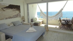 A bedroom with a bed, a nightstand, a lamp, a sofa, a dining table with chairs, and a view of the sea through large windows. - Lingon Silver Apartment, Wifi, AC, Balcony (Sesimbra)