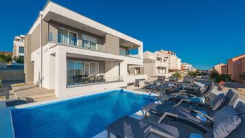 Relax by the pool surrounded by lounge chairs and sun loungers in this two-story building with large windows offering views of the surrounding area.