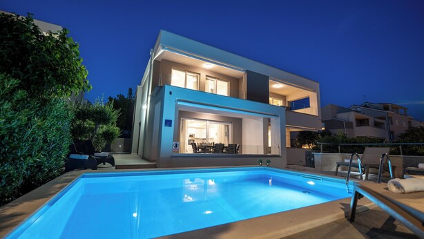 A modern two-story house with a swimming pool, outdoor seating, and a well-lit interior. - Apartments with Outdoor Heated Pool, Terrace and free WIFI (Novalja)