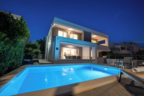 Una casa moderna de dos pisos con piscina, mobiliario exterior y un interior bien iluminado.