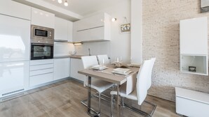 A modern kitchen with white cabinetry, stainless steel appliances, and a dining area with a wooden table and white chairs. - Apartments with Outdoor Heated Pool, Terrace and free WIFI (Novalja)
