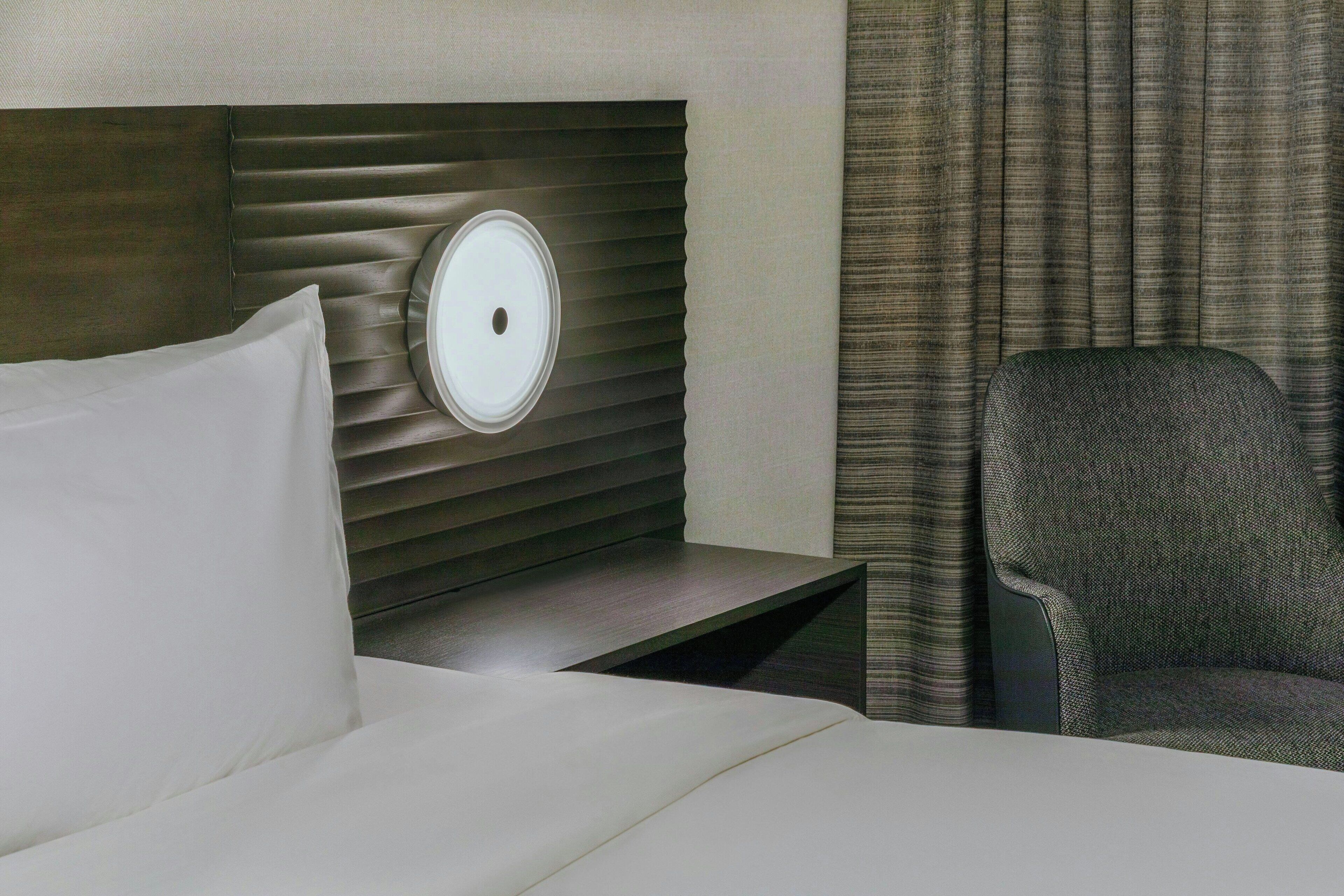 A hotel room with a bed, a nightstand, a lamp, a chair, and a curtain.