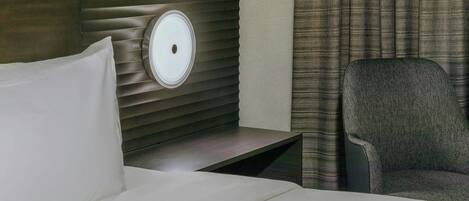 A hotel room with a bed, a nightstand, a lamp, a chair, and a curtain.