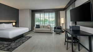 Une chambre d’hôtel avec un lit, un canapé, un bureau, une chaise, une télévision et une fenêtre avec des rideaux.