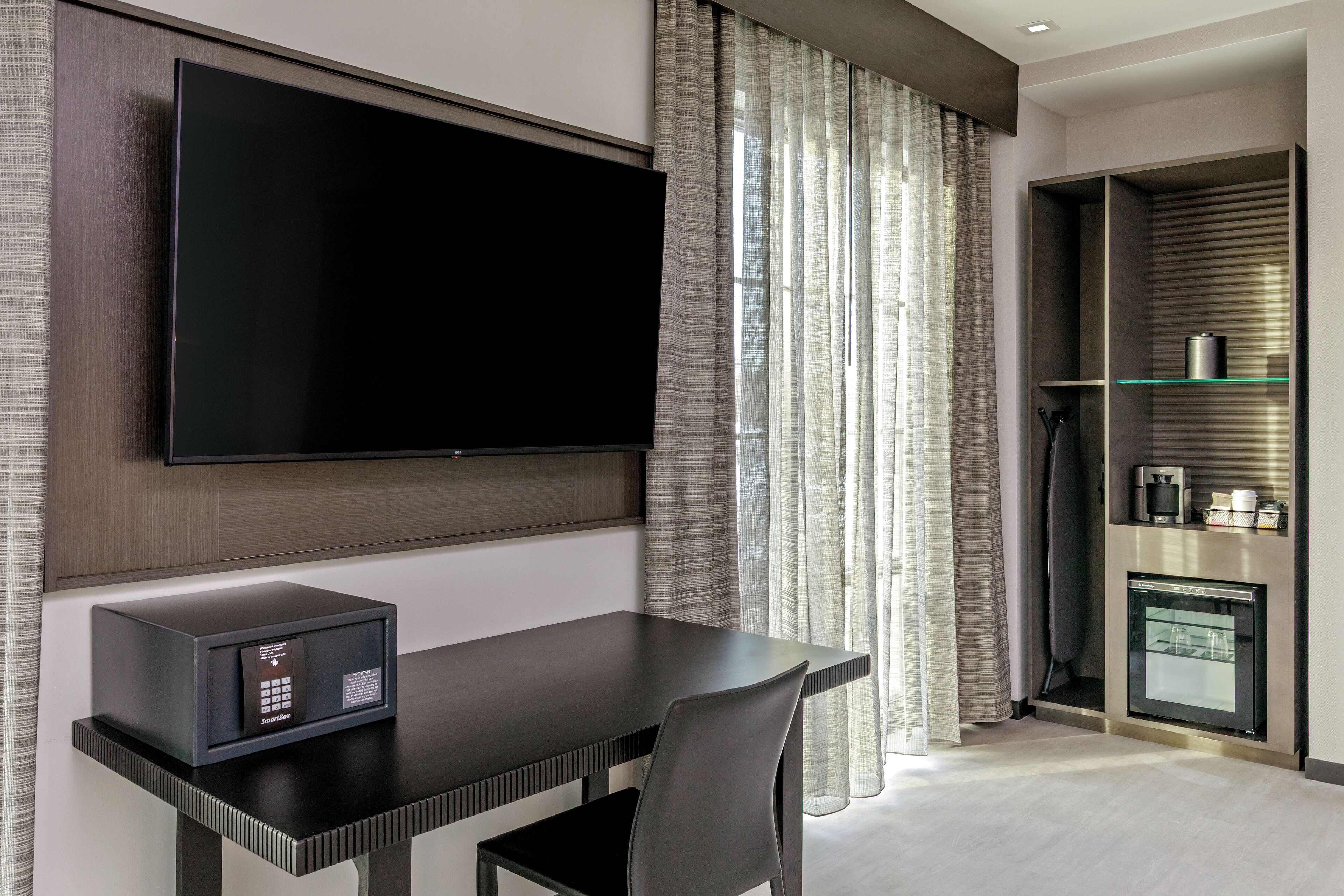Ein modernes Hotelzimmer mit einem flachbildfernseher an der Wand, einem kleinen Kühlschrank und einer Mikrowelle auf der Ablagefläche.