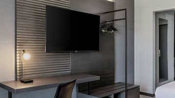 Una habitación de hotel moderna con una televisión de pantalla plana, un escritorio con lámpara, un perchero y una cama.