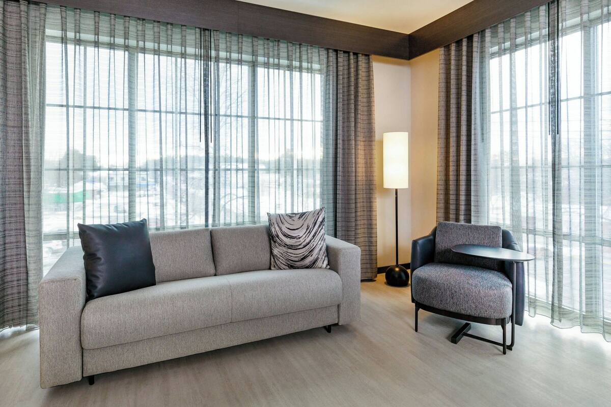 Una habitación de hotel moderna con sofá, sillón y lámpara.