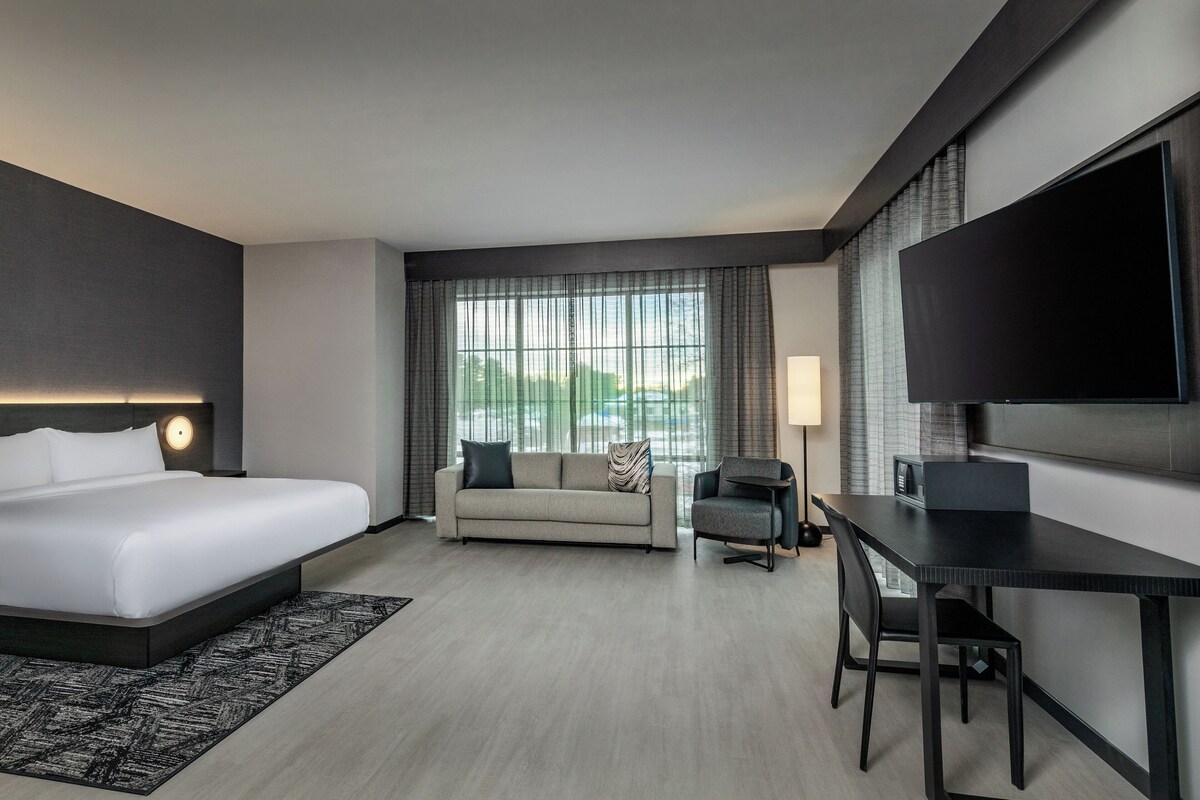 A modern hotel room with a bed, a sofa, a desk, and a TV.