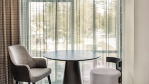 Une pièce moderne avec une table ronde et deux chaises, de grandes fenêtres avec des rideaux légers et un luminaire suspendu.