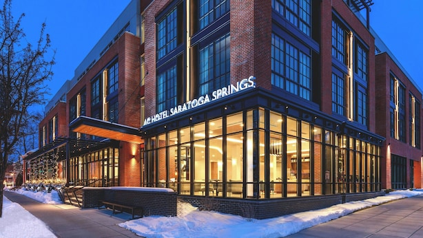 Un hôtel doté de grandes fenêtres, d’une façade en briques et d’une enseigne indiquant « ACHOTEL SARATOGA SPRINGS ».