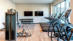 Une salle de sport équipée de tapis de course, d’une machine à presses pour les jambes et d’haltères.