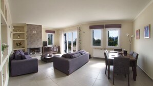 A spacious living room with a sofa set, a dining table with chairs, and a fireplace. - Spacious villa with privacy and mountain views, near Agia Efimia & Myrtos beach (Makriotika, Kefalonia)