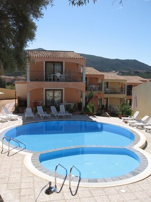 A swimming pool with lounge chairs and a two-story building with balconies.