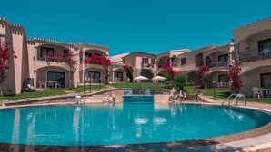 A swimming pool surrounded by a resort with multiple balconies, some with red flowers. - One bedroom apartment (4 people) - Residence Giardini di Badus (Badesi)