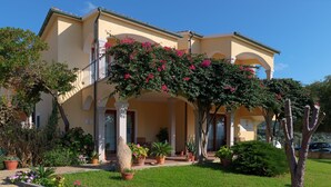 A two-story building with a balcony, potted plants, and a well-maintained lawn. - One bedroom apartment (4 people) - Residence Giardini di Badus (Badesi)