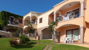 A multi-story building with balconies, a patio area with outdoor seating, and a stone archway. - One bedroom apartment (4 people) - Residence Giardini di Badus (Badesi)