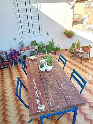 A wooden table with chairs, surrounded by potted plants, on a tiled patio. - The attic of the sculptor (Niscemi)