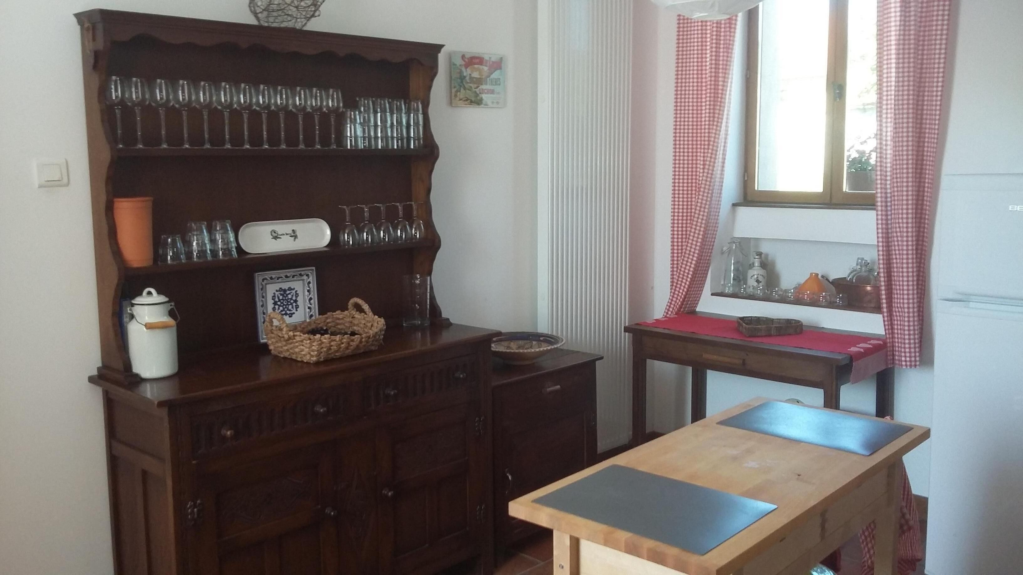 Een keuken met houten kastjes, een houten tafel en een raam met geruite gordijnen.