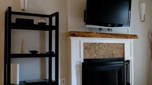 A living room with a fireplace, a mounted TV, and a black shelving unit.