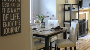 A dining area with a table set for two, a vase with flowers, and a motivational quote on the wall.