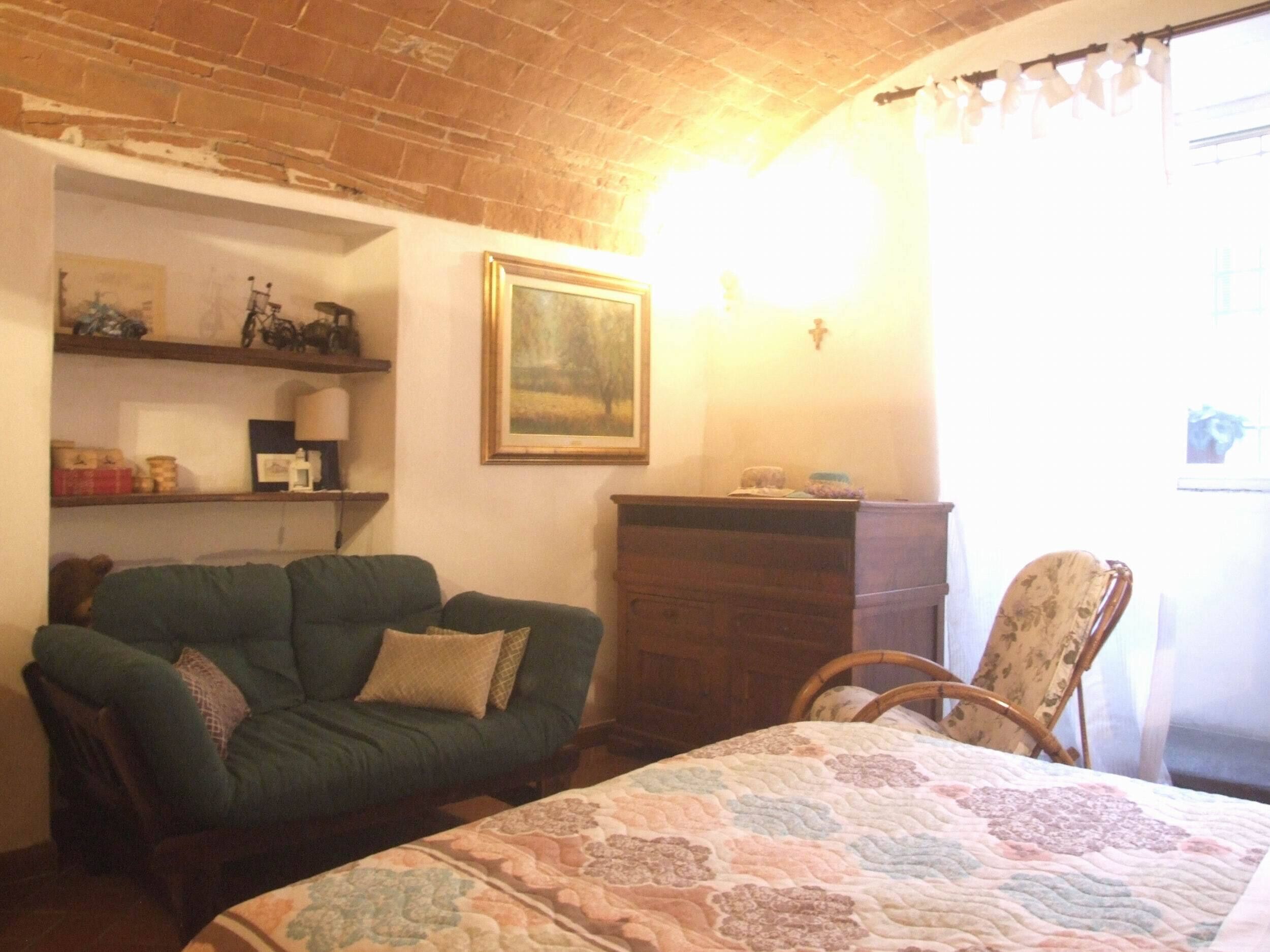 Een knus vertrek met een groene bank, een houten dressoir, een stoel en een bed met een bloemenquilt.