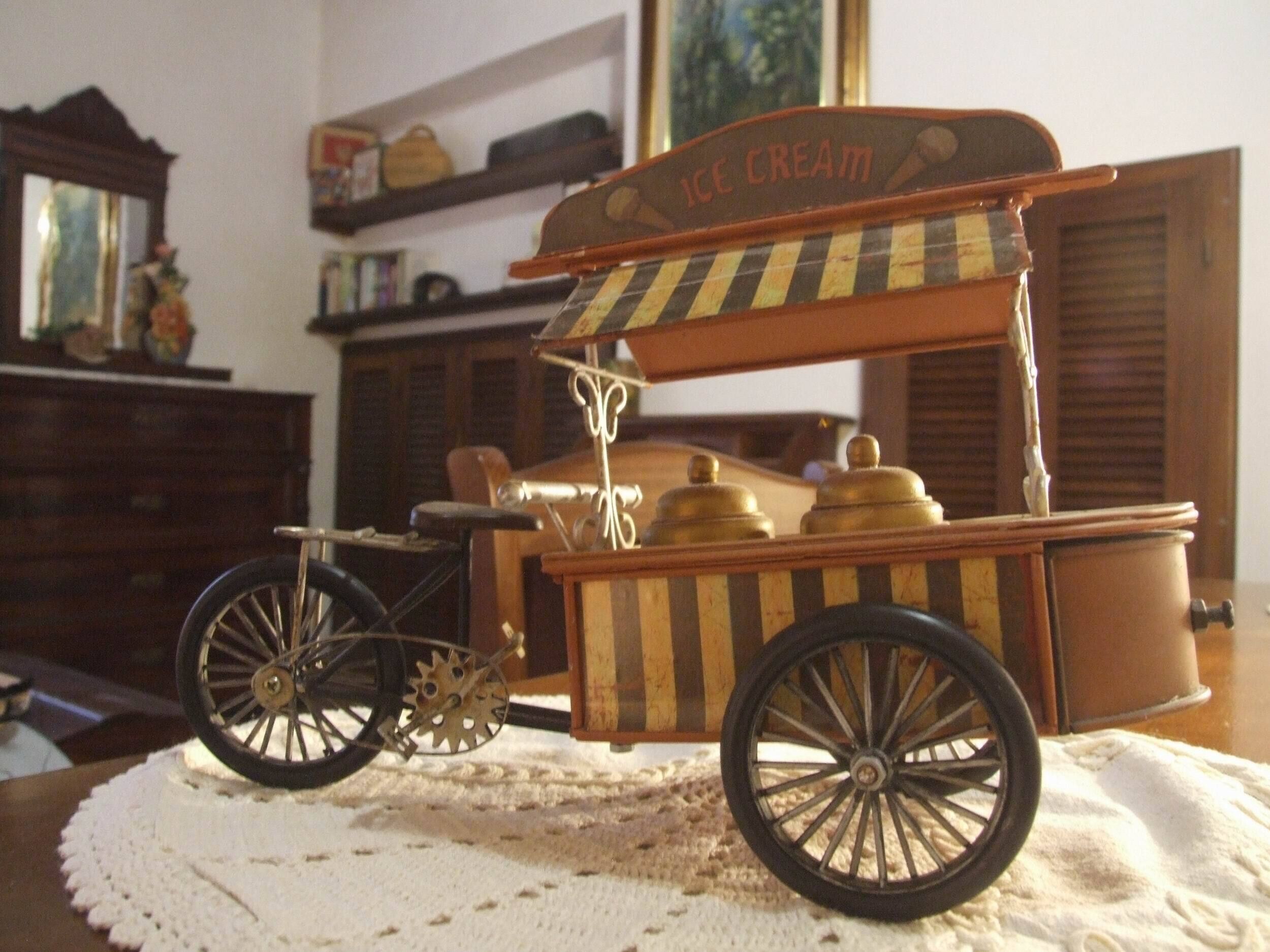 Un chariot à glaces d’époque, sur lequel est posée une table recouverte d’un chemin de table, et sur laquelle on peut lire l’inscription « GLACES ».