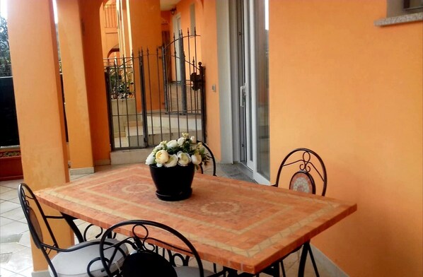 A dining area with a table and chairs, a potted plant, and a view of a gate and building in the background.