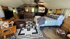 Un intérieur de chalet chaleureux et rustique, avec un lit, des meubles en bois, une petite cuisine et un ventilateur de plafond.