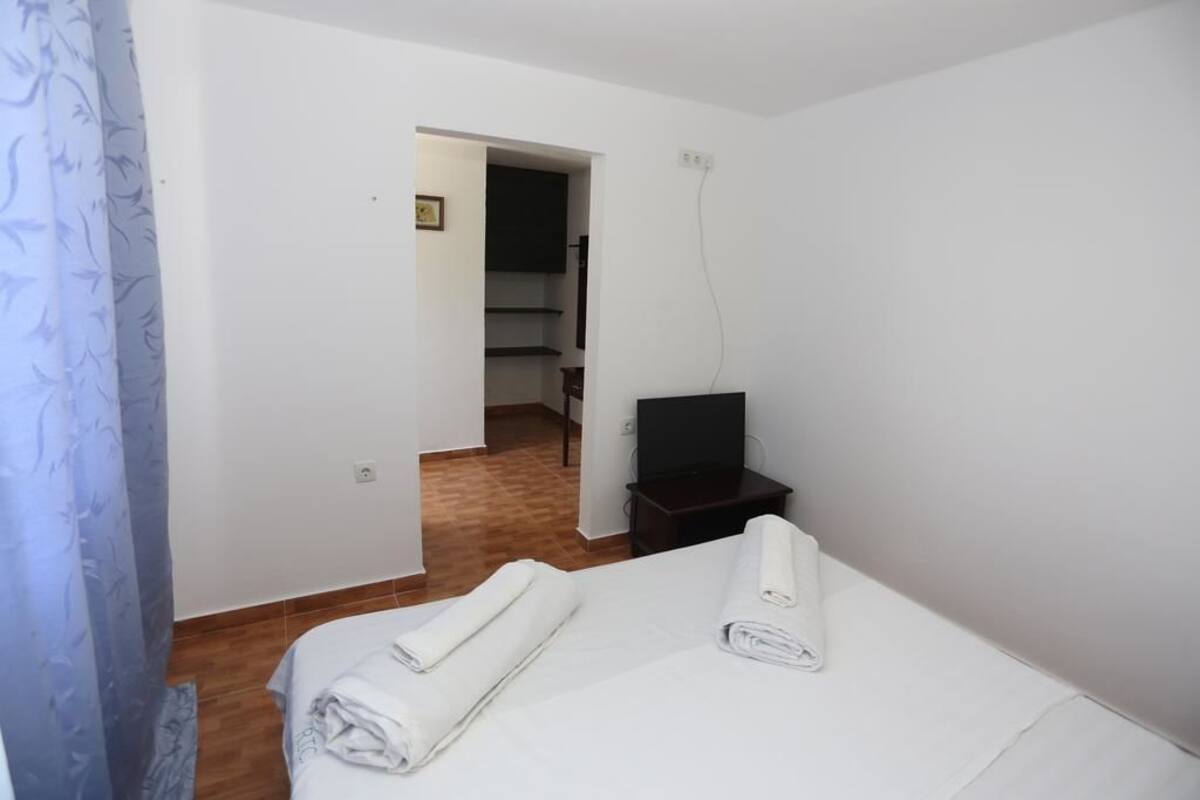 A hotel room with a bed, two rolled towels, a television on a small table, and a wooden floor.