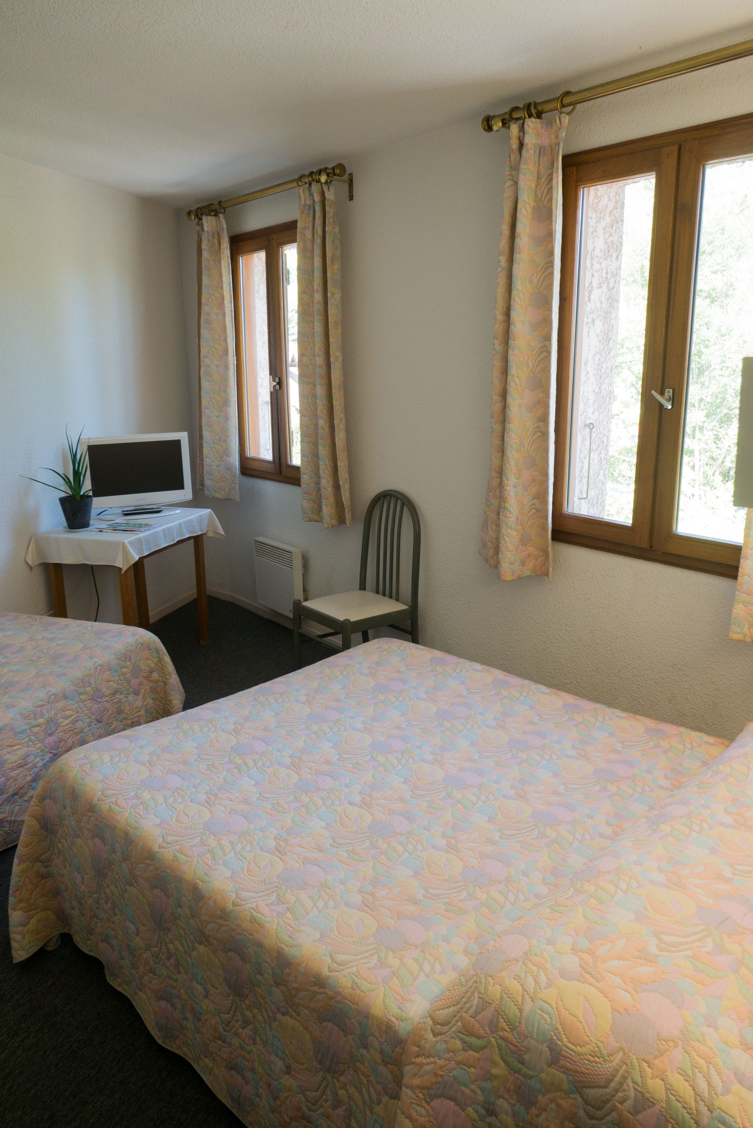 A room with two beds, a desk with a computer, a chair, and a window with curtains.