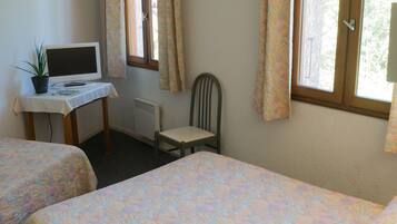 A room with two beds, a desk with a computer, a chair, and a window with curtains.