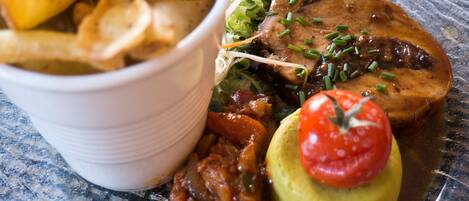 Un repas composé de différents plats, notamment un morceau de viande, des pommes de terre et une tomate servie dans un pain.