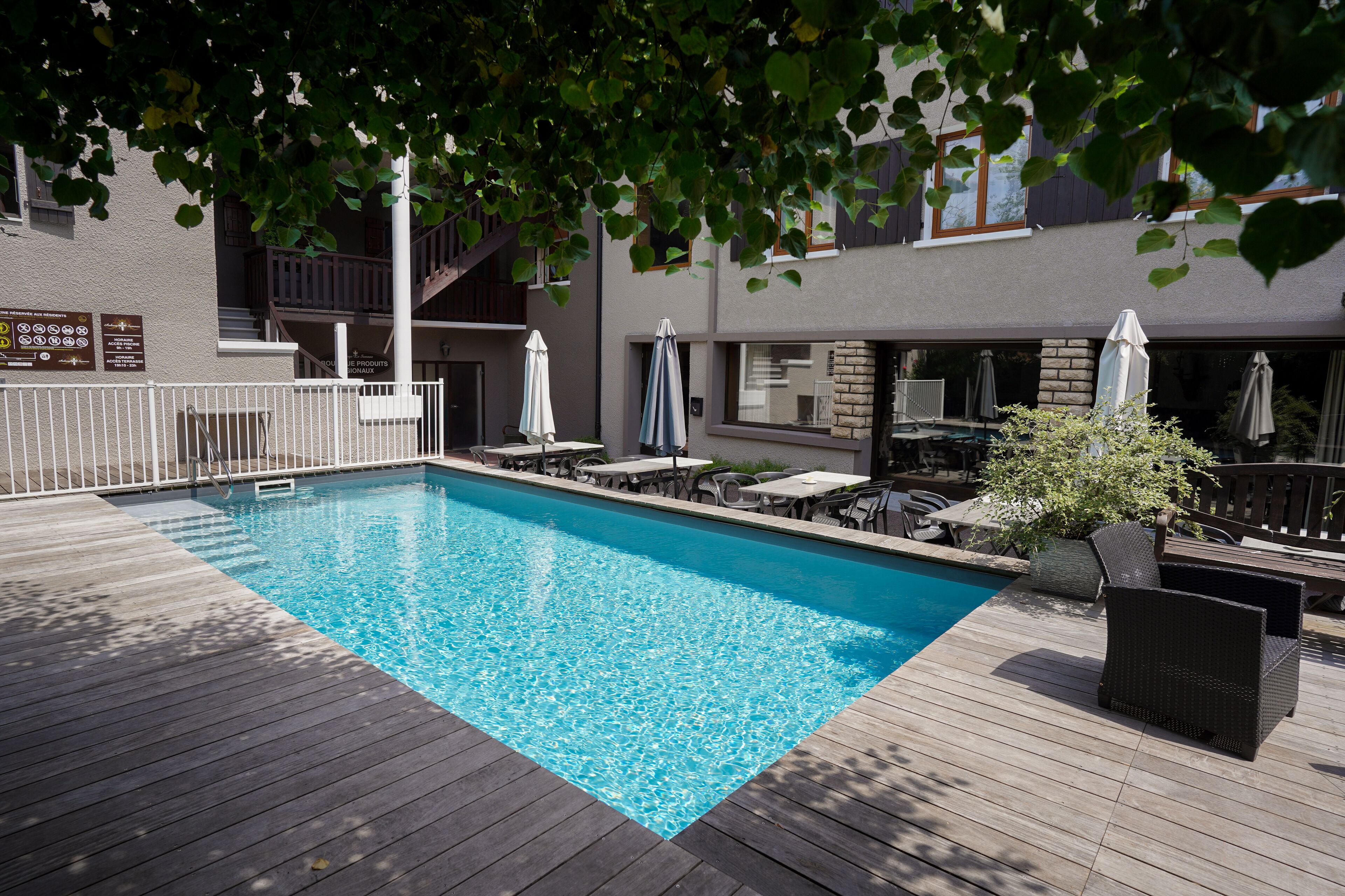 A swimming pool with a wooden deck, outdoor seating, and a staircase leading to an upper level.