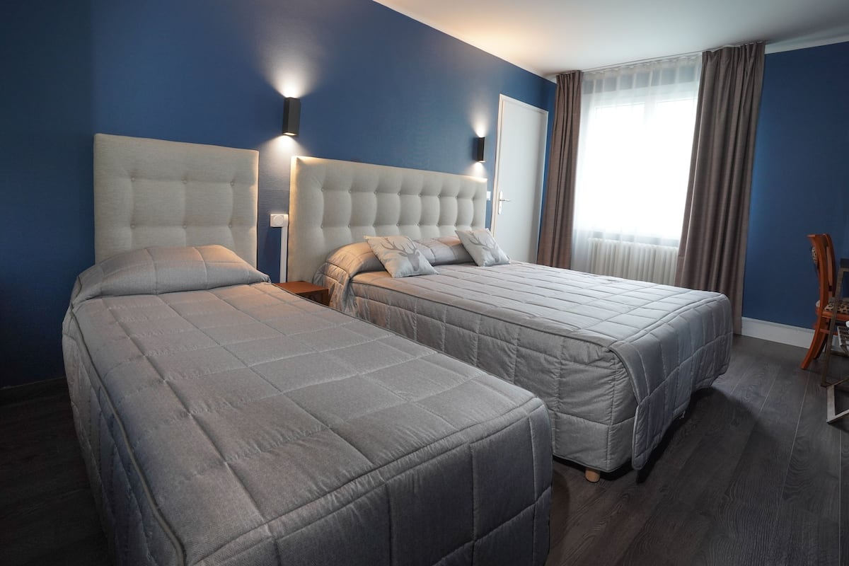 Ein Hotelzimmer mit zwei Betten, einem großen Kopfteil und einem Fenster mit Vorhängen.