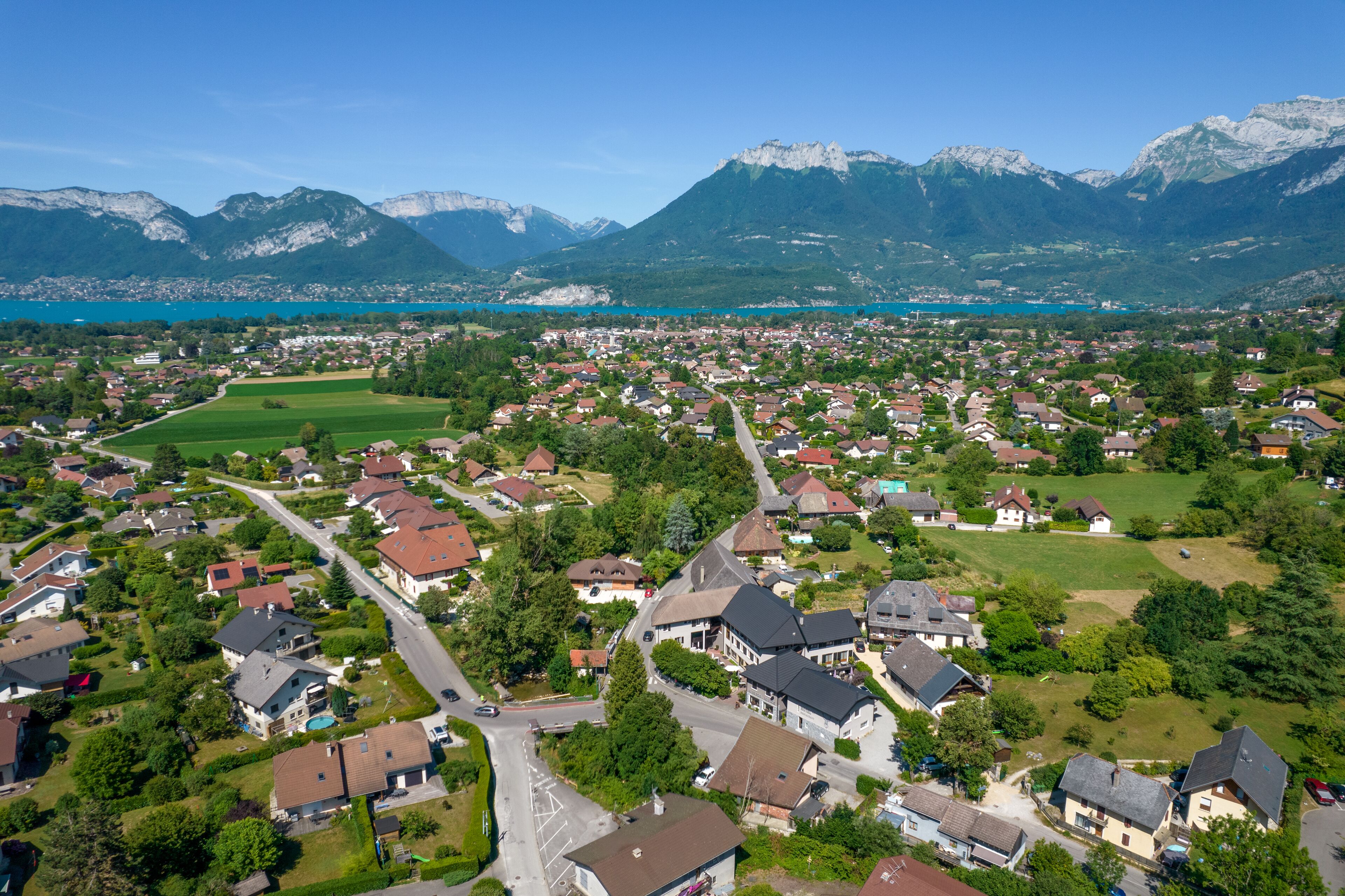 An aerial view of a residential area with houses, roads, and a lake surrounded by mountains.