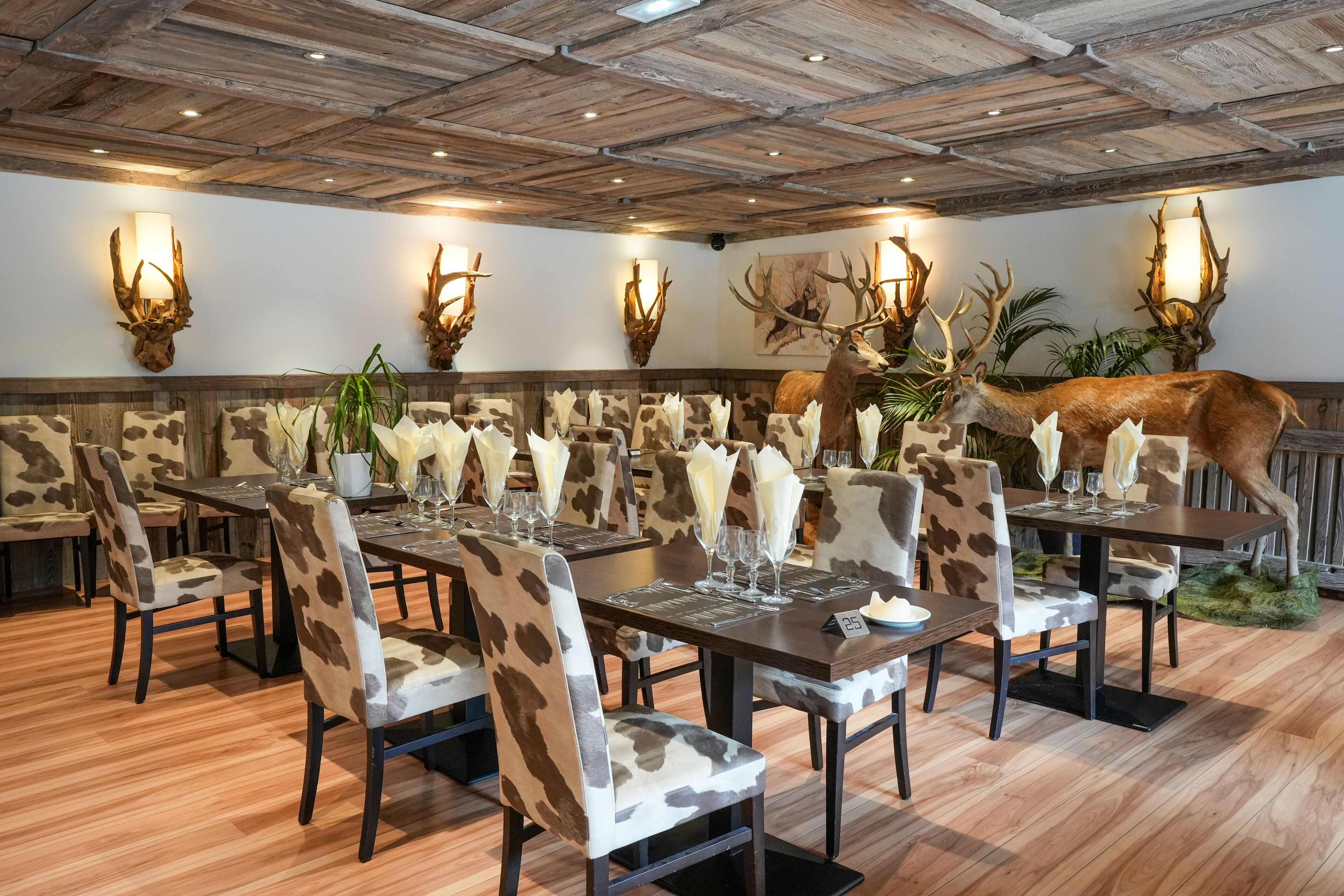 A restaurant with wooden ceiling and walls, antler wall sconces, and a deer head decoration.