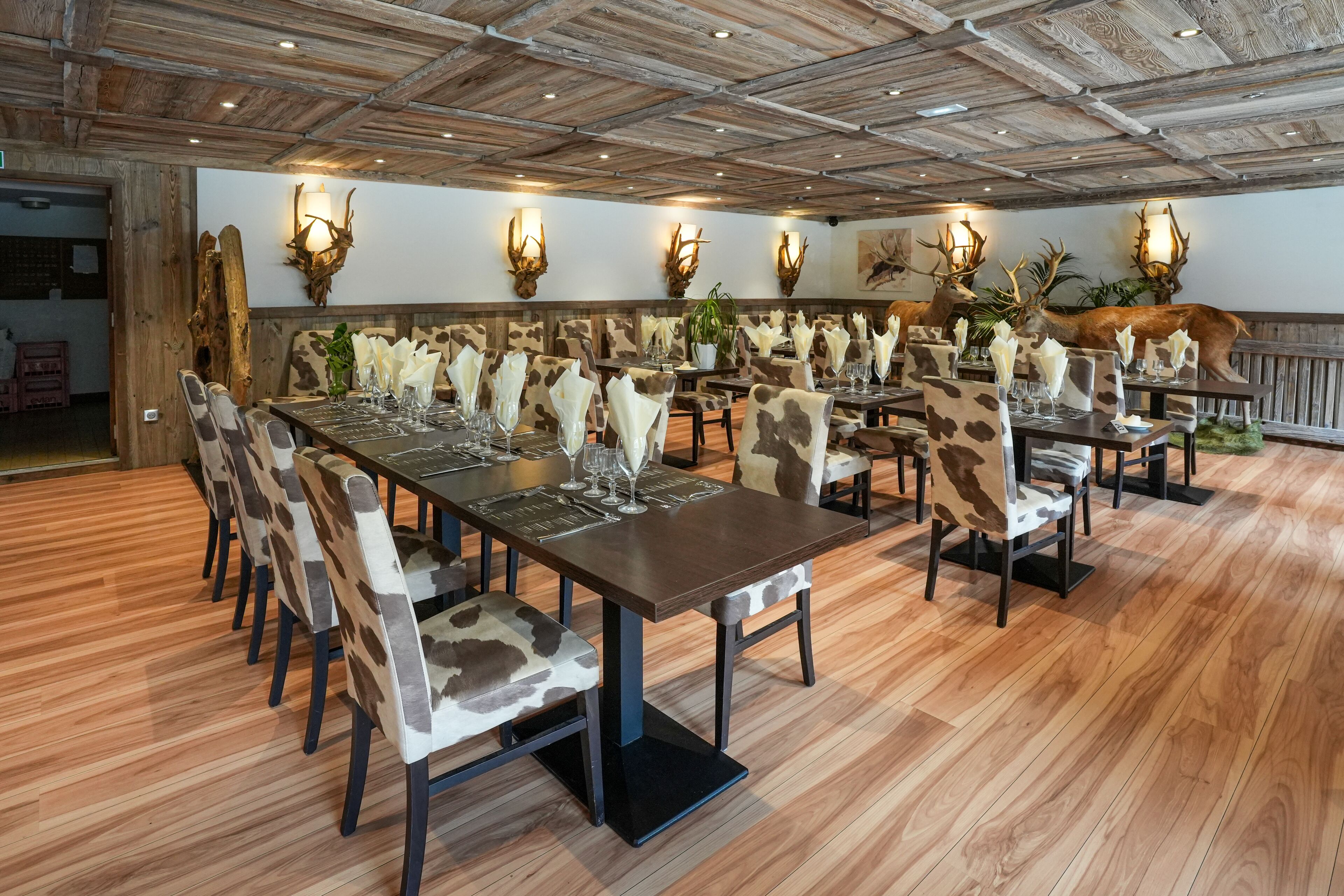 Een restaurant met houten vloeren, tafels gedekt met witte servetten en stoelen met een camouflageprint.