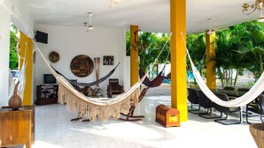 A spacious outdoor area with a hammock, chairs, and a table, surrounded by yellow pillars and a view of greenery. - Hotel San Basilio de Palenque (Mahates)