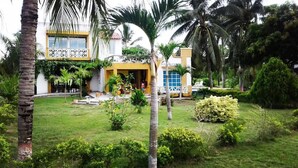 A house with a well-maintained lawn, palm trees, and a yellow and white exterior. - Hotel San Basilio de Palenque (Mahates)