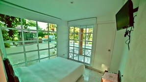 A room with a bed, large windows, a TV, and a small table. - Hotel San Basilio de Palenque (Mahates)