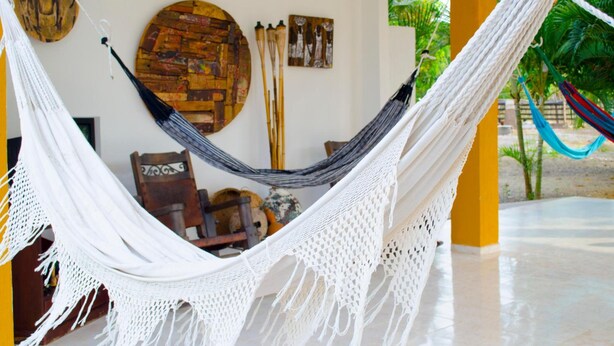 A hammock in a room with a rustic wall decor, a wooden chair, and a tiled floor. - Hotel San Basilio de Palenque (Mahates)