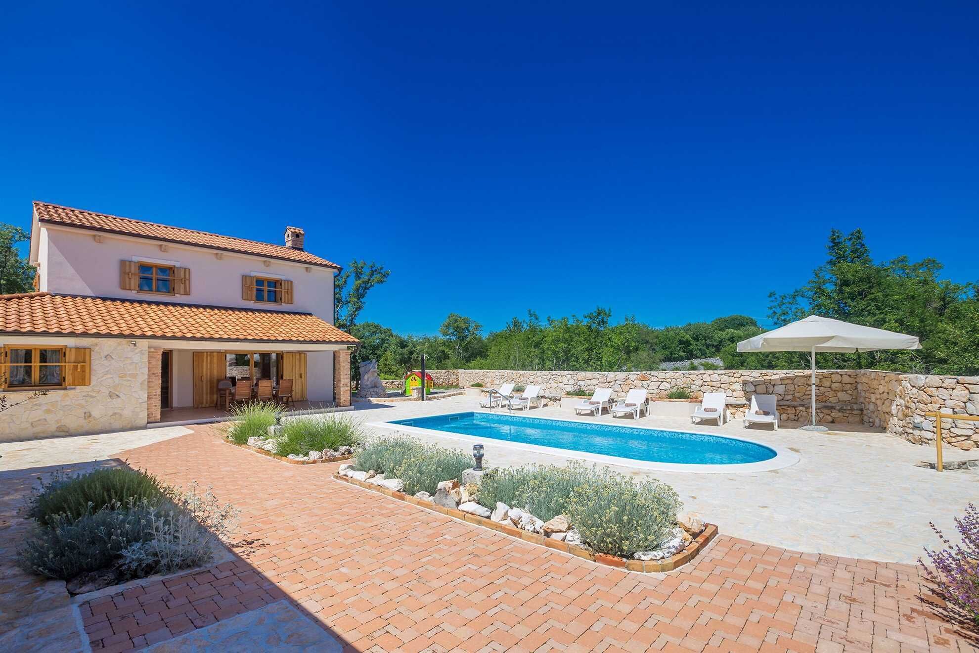 Une maison à deux étages avec une piscine, un espace salon extérieur et un mur en pierre.