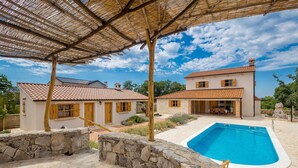 Eine Villa mit Swimmingpool, Steinmauern und einer überdachten Terrasse.
