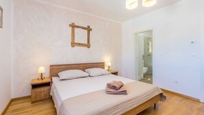 Ein Schlafzimmer mit einem hölzernen Bett, zwei Nachttischen mit Lampen, einer Holz Kopfteil und einem Spiegel an der Wand. Eine Badezimmertür ist ebenfalls zu sehen.
