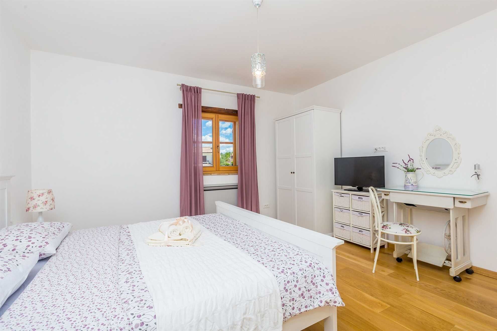 A bedroom with a bed, a desk with a chair, a television, and a wardrobe.