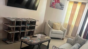 A living room with a sofa, a coffee table, a TV, and a bookshelf. - Island Turquoise Rental- Spacious Two bedroom & 2 Bathroom (Providenciales)