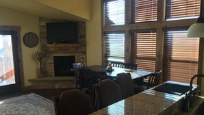 Un comedor con chimenea de piedra, persianas de madera y un televisor montado encima.